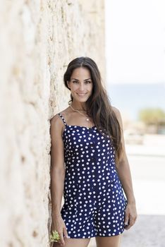 Beautiful smiling woman in blue dress leaning on wall while looking camera