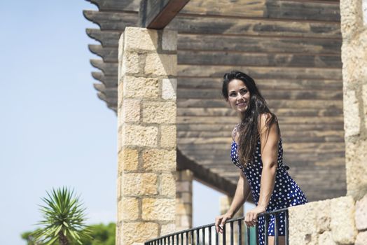 Beautiful smiling woman in blue dress leaning on fence while looking away