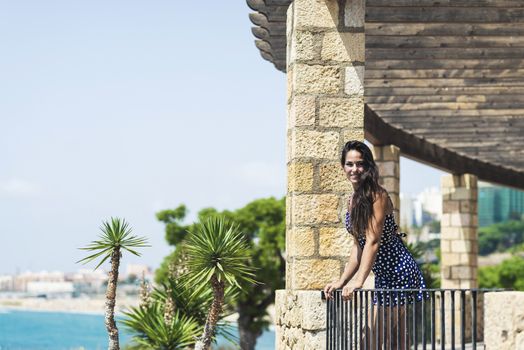 Beautiful smiling woman in blue dress leaning on fence while looking away