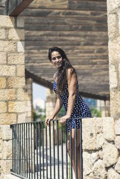 Beautiful smiling woman in blue dress leaning on fence while looking away