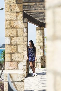 Beautiful smiling woman in blue dress leaning on wall while looking away