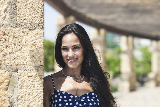 Beautiful smiling woman in blue dress leaning on wall while looking away