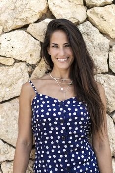 Beautiful smiling woman in blue dress leaning on wall while looking camera
