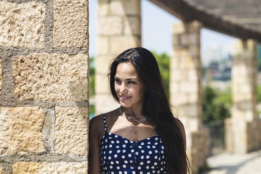 Beautiful smiling woman in blue dress leaning on wall while looking away