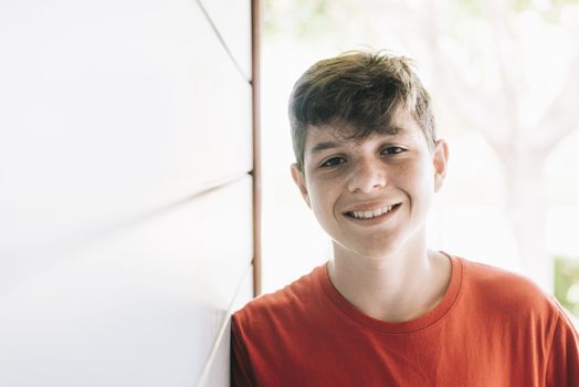 Portrait of a cheerful male teen leaning on wood wall while looking camera in a sunny day