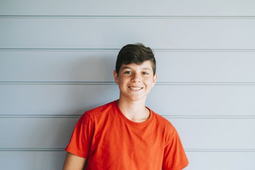 Portrait of a cheerful male teen leaning on wood wall while looking camera in a sunny day