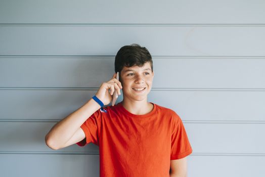 Young teen with red t-shirt standing against wall while using phone