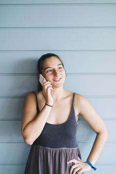 Attractive young adult female in summer dress talking on cell phone while leaning against wood paneled wall