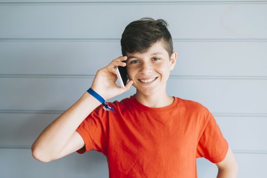 Young teen with red t-shirt standing against wall while using phone