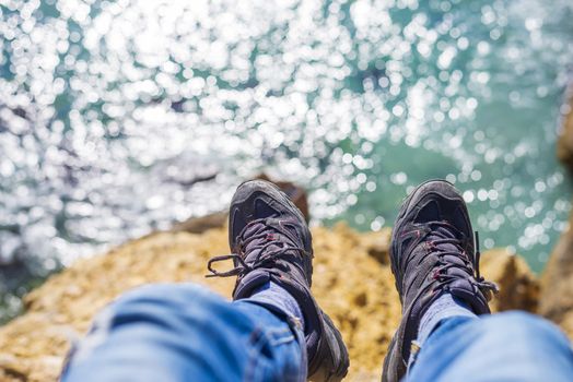 Young brave man sitting on a high cliff above calm sea