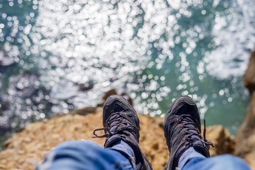 Young brave man sitting on a high cliff above calm sea