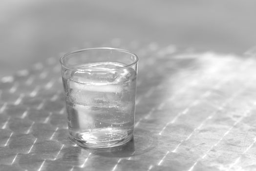 Glass of water with ice on a metallic table outdoors in a bright day