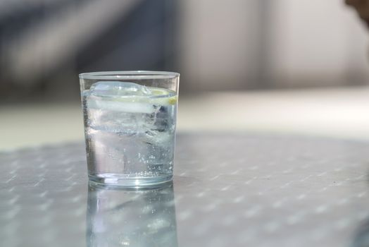 Glass of water with ice on a metallic table outdoors in a bright day