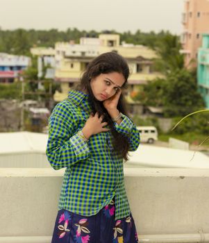 Sexy and romantic Indian girl with moist eyes and dressed in green shirt and hair scattered with red and gorgeous red lips and standing on the roof of the house in the open environment