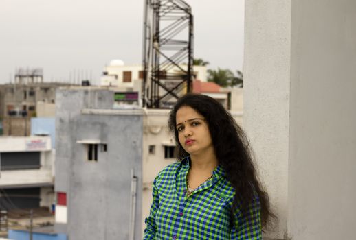 Hindu young Indian girl in green and blue shirt standing near white pole and in a long open thick hair