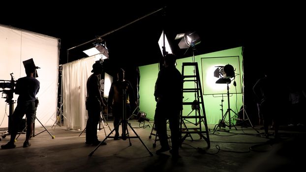 Low key silhouette lighting of VDO production behind the scenes which film crew team are setting up camera and set for shooting and waiting for movie director okay with the scenes in monitor.