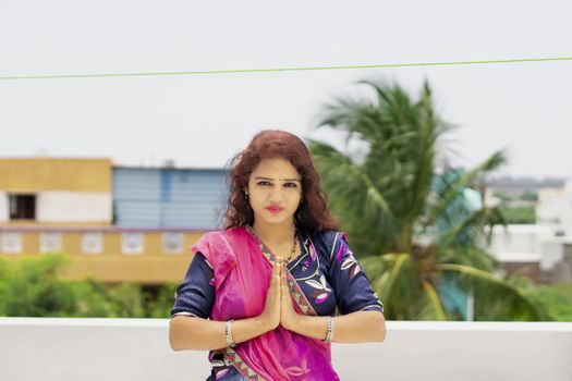 A beautiful Hindu girl and choli and lehenga dressed according to her custom and wearing lipstick on pink red lips and remembering God with blue gorgeous eyes and brown long open hair and folded hands