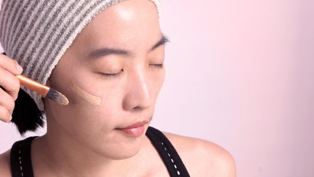 Asian girl or woman 40 years old beautiful face with japanese look making up by foundation liquid and cosmetic brush on sensitive skin for helping her complexion look flawless and real no retouch