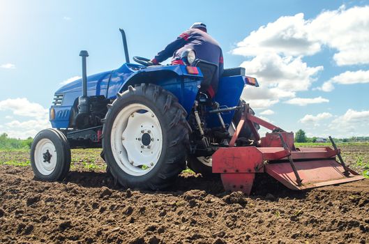 Farmer on a tractor with a milling machine processes loosens soil in the farm field. Preparation for new crop planting. Grind and mix soil on plantation. Loosening surface, cultivating the land.