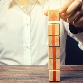 Businessman builds a tower of blocks with an up arrow. Career promotion, growth of professional skills. Profit growth. Marketing. Improving efficiency. Business development, expansion improvement.