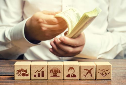 A man is counting money on the background of blocks with business attributes. Investments. Calculation of the total profit. Success, high profitability. Effective business model