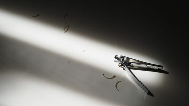 Close-up images of nail clipper from top view angle after cut out sensitive damage nails from hands and fingers and lay down on the floor and have sun light shade and shadow on it.