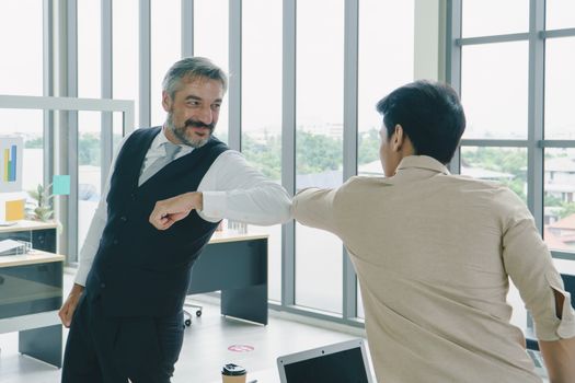 Senior businessmen greet young businesses by hitting elbow instead shake hand, smiling, and having a friendly at office.  concept together teamwork, protection, and social distancing are new normal