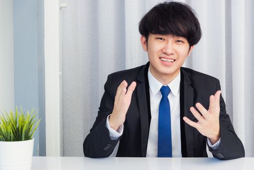 Work from home, Close up face of Asian young businessman video conference call or facetime he looking to camera raises hands to explain about his job to team on a desk at the home office