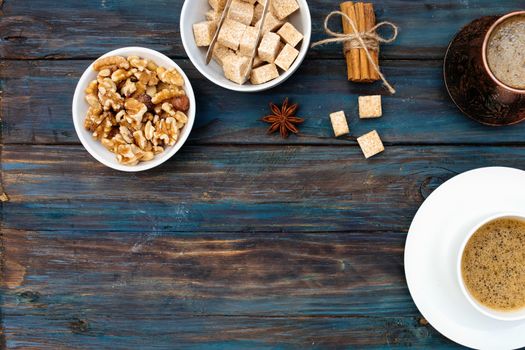 Nuts in the bowl, coffeepot, cinnamon, anise, sugar and cap of coffee on wooden background