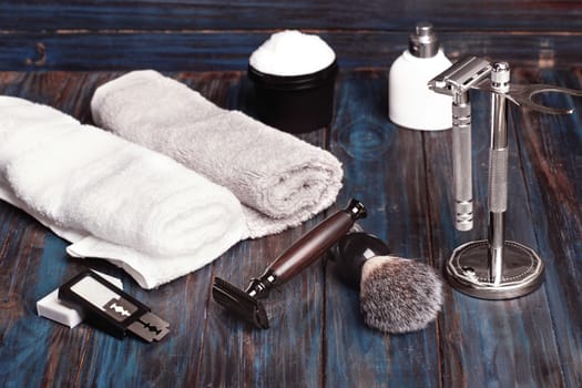 Razors, brush, blade, stand, perfume and towels on a wood background.