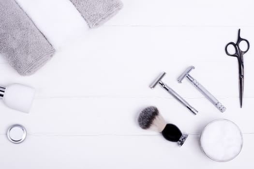 Razors, brush, balsam, perfume, towels and scissors on a wood background.