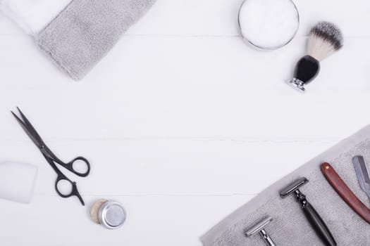 Razors, brush, balsam, perfume, towels and scissors on a wood background.