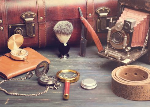 old fashioned objects brush, suitcase, compass, razor, watch, old camera, magnifying glass, balsam, leather belt on a wooden background