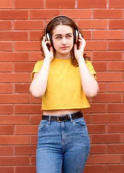 young woman wearing yellow shirt listening to music with headphones against brick wall