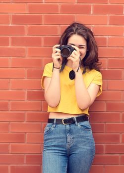 young woman wearing yellow shirt, taking photos against brick wall