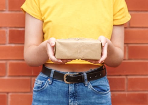 young woman wearing yellow shirt, holding gift against brick wall