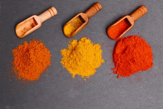 Colorful spices and wooden spoon on black background