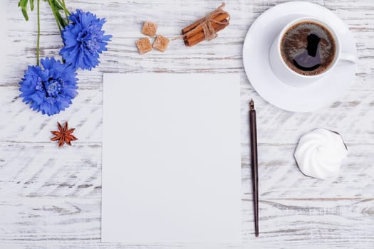 Mockup of empty paper, a white cup of coffee, flower, ink pen, cake, sugar, anise and sinnamon on white wood desk. Flat Lay with no people. View from the top.