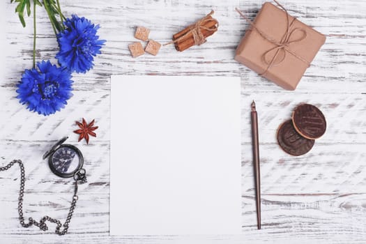 Mockup of empty paper, flower, ink pen, cakes, sugar, anise and gift on white wood desk. Flat Lay with no people. View from the top.