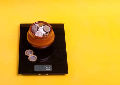 A pot full of coins on a scale on a yellow background