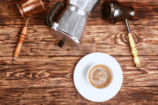 A cup of coffee and different coffee pots on wooden table