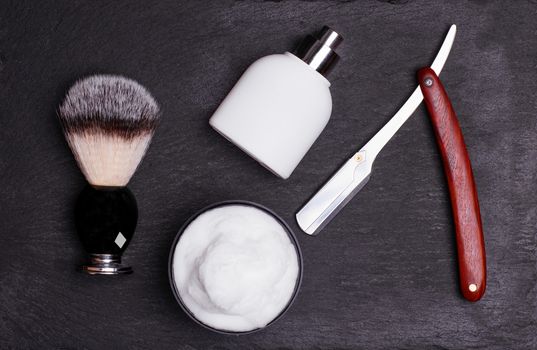 Razor, brush, perfume, balsam and shaving foam on a black background.