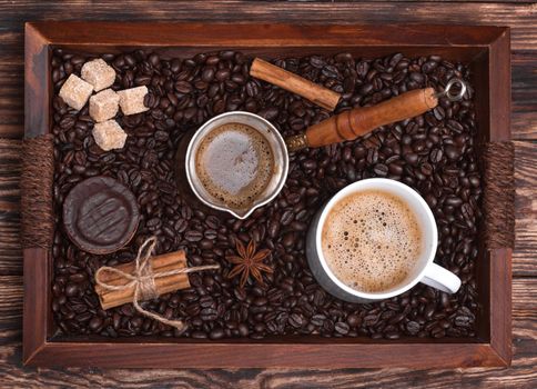 Cup of coffee, coffeepot, biscuit, cinnamon, anise, sugar, coffee beans on a wooden tray. View from the top.