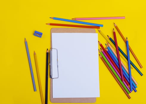 Mockup for drawing and painting, multi-colored pencils and sharpener, empty paper on yellow background