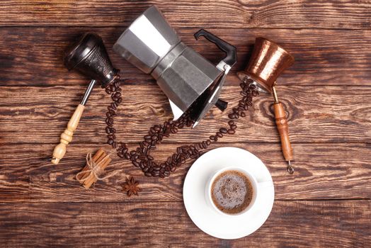 Cup of coffee, three coffeepots, cinnamon, anise, coffee beans on a wooden tray. View from the top.