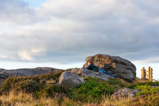 Man laying on stone and taking photos of the landscape on phone against cloudy sky