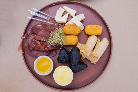 Beer snacks on a clay plate: bastruma, feta cheese, cheese in batter, honey and mustard.