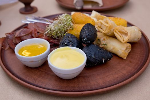 Beer snacks on a clay plate: bastruma, feta cheese, cheese in batter, honey and mustard. Soft focus.