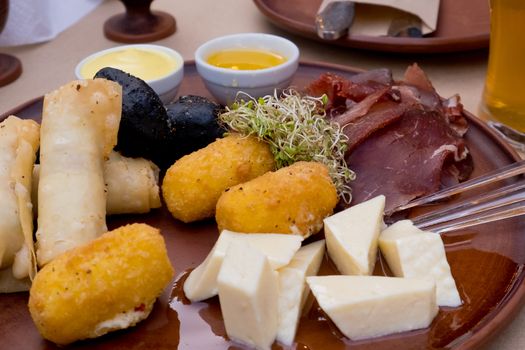 Beer snacks on a clay plate: bastruma, feta cheese, cheese in batter, honey and mustard. Selective focus.