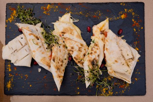 Lavash with cheese on a flat black plate decorated with micro green and pomegranate seeds. Restaurant dish.